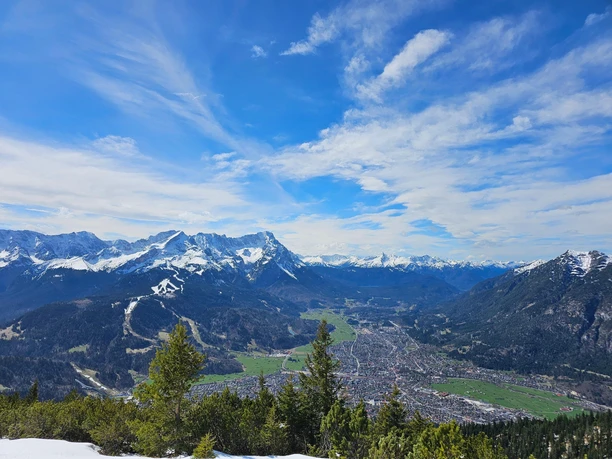 Blick auf Garmisch-Partenkirchen Blick von oben auf Garmisch-Partenkirchen vor schneebedeckten Bergen unter blauem Himmel
