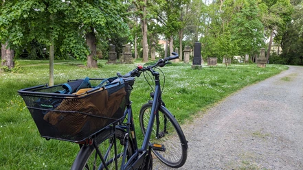 WF-Alter-Friedhof.jpg Ein Fahrrad ist an einer Wiese mit historischen Grabsteinen geparkt.