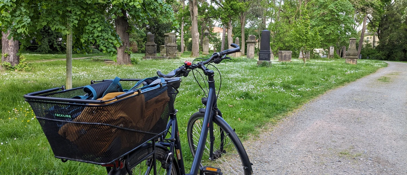 WF-Alter-Friedhof.jpg Ein Fahrrad ist an einer Wiese mit historischen Grabsteinen geparkt.