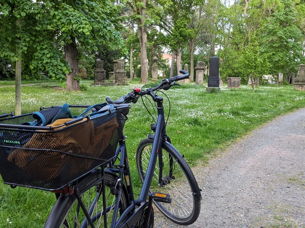 WF-Alter-Friedhof.jpg Ein Fahrrad ist an einer Wiese mit historischen Grabsteinen geparkt.