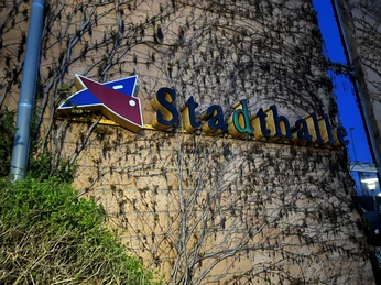 Ein bewachsener Außenbereich der Stadthalle Verden bei Dämmerung, mit markantem Schriftzug an der Fassade.