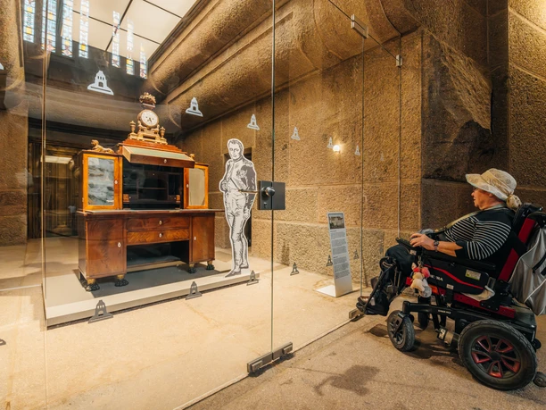 Une personne en fauteuil roulant observe une pièce d'exposition de l'époque napoléonienne derrière une vitre à l'intérieur du monument de la bataille des Nations, curiosités, histoire