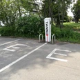 e-Tankstelle in Lindlar-Linde <p>Elektroladestation auf einem Parkplatz in Lindlar, umgeben von grünen Büschen und einem Gehweg.</p>