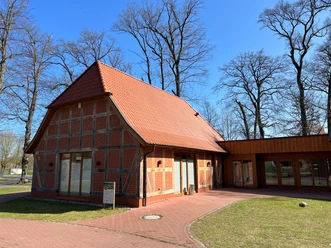 Rövers Schafstall Backsteinfachwerkhaus mit rotem Satteldach, umgeben von kahlen Bäumen und sonnigem, blauem Himmel.