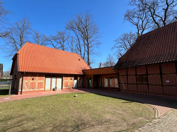 A traditional sheep barn with red bricks, surrounded by bare trees under a bright blue sky.