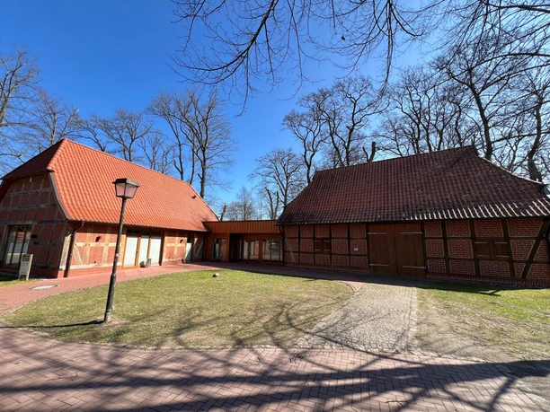Two historic half-timbered buildings with red-tiled roofs, surrounded by trees under a clear sky.