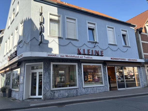 Herford-Café Kleine-Pro Herford GmbH (42).jpeg Zweistöckiges Café mit blauer Fassade, großen Fenstern, rotem Schriftzug "KLEINE" und Getränkeangebot.