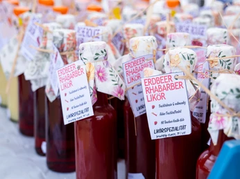 Bürgeler Hofmarkt 2025 Flaschen mit Erdbeer-Rhabarber-Likör auf einem Tisch, umgeben von handgefertigten Etiketten.