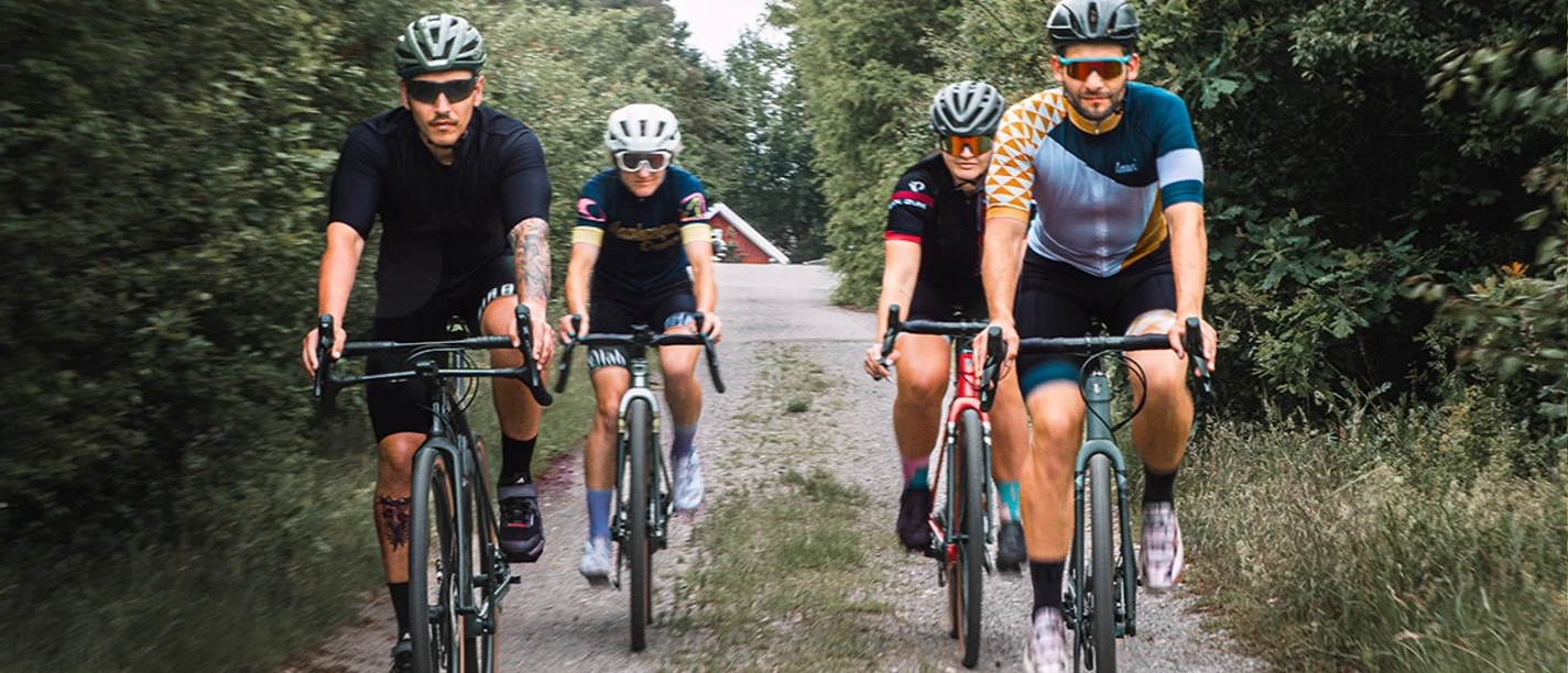 Vier Radfahrer in Sportbekleidung fahren nebeneinander auf einem schmalen Waldweg.