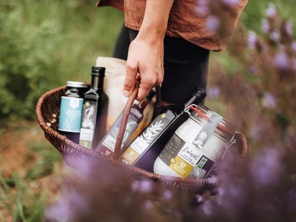Ölmühle Solling Produktkorb©Ölmühle Solling_Maike Wittreck.jpg Ein geflochtener Korb voller feinster Öle und Gewürze von der Ölmühle Solling, gehalten von einer Person.