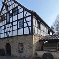 Rindersberger Mühle in Essen Fachwerkhaus aus Stein und Holz mit Wasserrad, umgeben von Bäumen, unter sonnigem Himmel.
