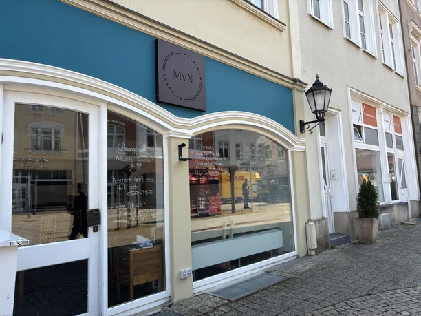 Großes Schaufenster eines Cafés mit türkisfarbenem Vordach und stilvoller Außenbeschriftung.