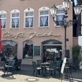 Café Jach mit rotem Sonnenschirm und Außensitzbereich, historische Hausfassade und Straßenlaternen.