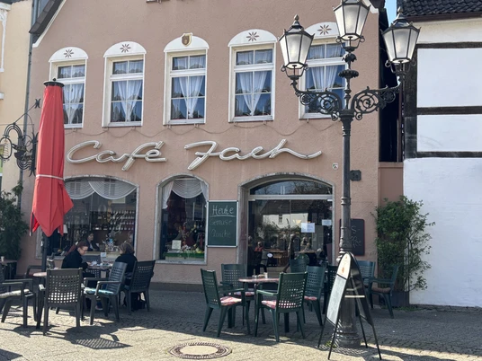 Café Jach mit rotem Sonnenschirm und Außensitzbereich, historische Hausfassade und Straßenlaternen.