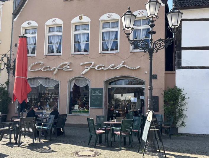 Café Jach mit rotem Sonnenschirm und Außensitzbereich, historische Hausfassade und Straßenlaternen.