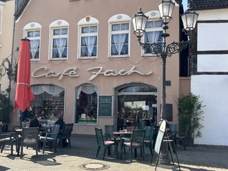 Herford-Café Jach-Pro Herford GmbH (75).jpeg Café Jach mit rotem Sonnenschirm und Außensitzbereich, historische Hausfassade und Straßenlaternen.