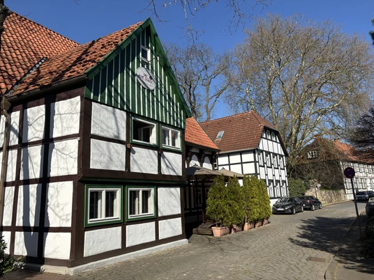 Herford-Die Alte Schule-Pro Herford GmbH (22).jpeg Fachwerkhäuser mit roten Ziegeldächern und historischen Details säumen eine gepflasterte Straße.