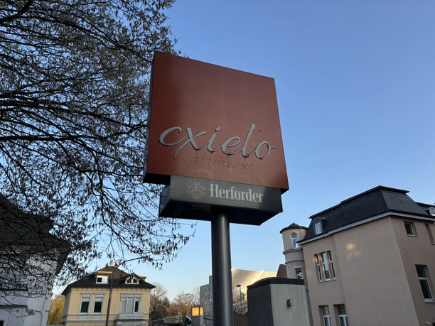 Herford-Cxielo-Pro Herford GmbH (11).jpeg Ein Schild mit der Aufschrift „Cxielo Barrestaurant“ und „Herforder“ steht vor moderner Architektur.