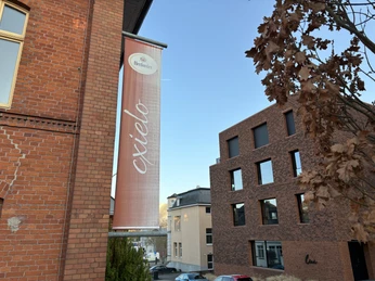 Herford-Cxielo-Pro Herford GmbH (12).jpeg Werbebanner der Marke Herforder hängt an einer roten Backsteinfassade, umgeben von modernen Gebäuden.