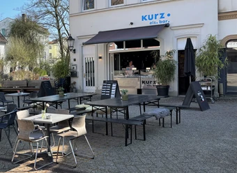 Herford-Kurz Eis Bar-Pro Herford GmbH (60).jpeg Eisbar mit Außensitzbereich, moderner Einrichtung und einladendem Ambiente unter blauem Himmel.