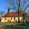 St. Jacobi-Kirche Husum Gelbe Kirche mit rotem Dach und Turm, umgeben von Bäumen auf grünem Rasen unter blauem Himmel.