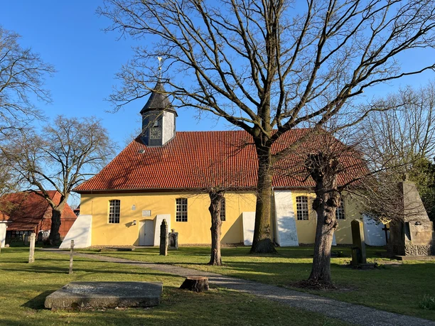 St. Jacobi-Kirche Husum Gelbe Kirche mit rotem Dach und Turm, umgeben von Bäumen auf grünem Rasen unter blauem Himmel.