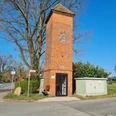 Trafoturm Brokeloh Roter Backsteinturm mit bogenförmigen Fenstern, umgeben von einem Stromkasten und einer Sitzbank an der Straße.