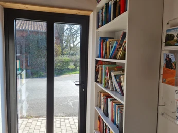 Trafoturm Brokeloh Durch die Glastür strömt Licht in den kleinen Raum mit Bücherregalen, die vielfältige Literatur bieten.