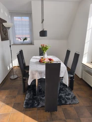 Essbereich.jpg Moderner Essbereich mit Tisch, sechs Stühlen, Tulpenvase und Obstschale vor einem Fenster.