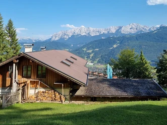 St.-Martins-Hütte am Grasberg Holzhütte am Hang mit Holzstapeln und Bergblick, daneben Terrasse mit Stühlen vor Alpenkulisse.