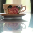 Ostfriesenteetasse Klassische Ostfriesentasse mit rosa Rosenmuster auf einer spiegelnden Tischplatte.