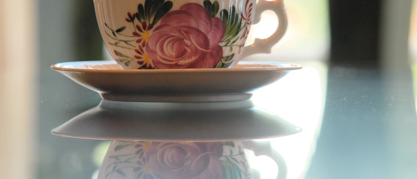 Ostfriesenteetasse Klassische Ostfriesentasse mit rosa Rosenmuster auf einer spiegelnden Tischplatte.