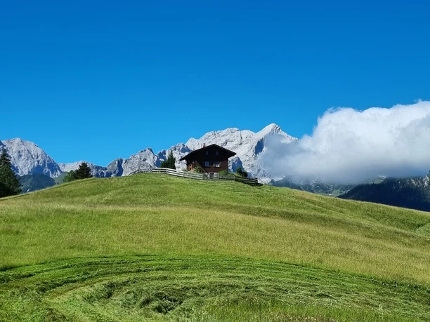 Eckbauer Holzhütte auf weiter Bergwiese vor hellen Felsgipfeln und einer vorbeiziehenden Wolke