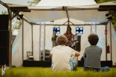 Frotheim Open Air Zwei Personen sitzen mit dem Rücken zu uns vor einer OpenAir Bühne im Gras