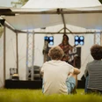Frotheim Open Air Zwei Personen sitzen mit dem Rücken zu uns vor einer OpenAir Bühne im Gras