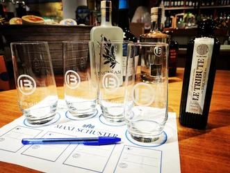 Tastings_Maxi Schuster.jpg Verschiedene Gin-Flaschen und Gläser auf einem Tisch bei einer Degustation, im Hintergrund Regale.