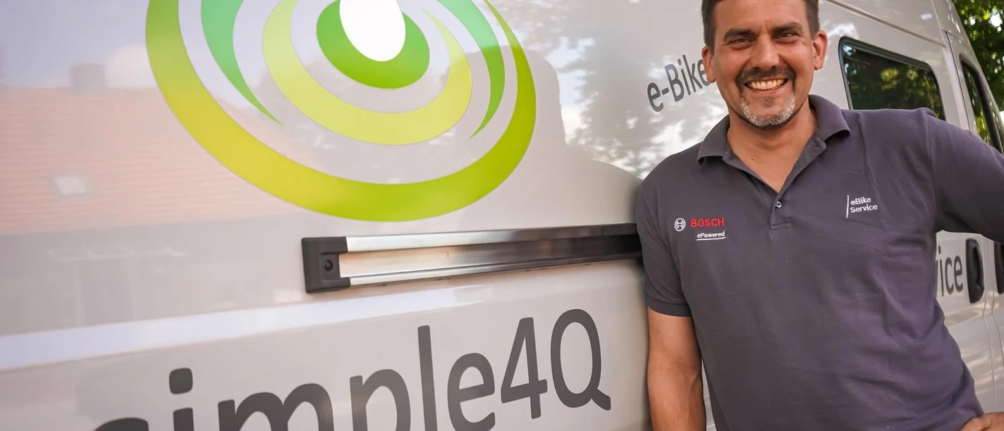 simple4Q.jpg Ein lächelnder Mann lehnt an einem weißen Van mit dem Logo "simple4Q".