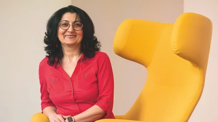 Ruzanna Shahinyan Ruzanna Shahinyan sitzt lächelnd neben einem großen, modernen gelben Sessel. Sie trägt eine rote Bluse.
