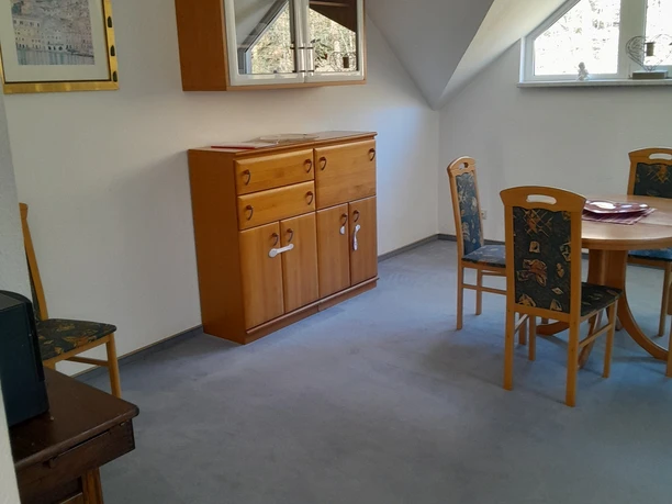 Ferienwohnung Preyersmühle Heller Essbereich mit Holzmöbeln, darunter ein runder Tisch mit Stühlen und eine Vitrine an der Wand.