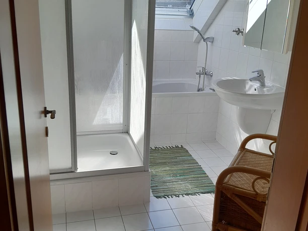Ferienwohnung Preyersmühle Das Bild zeigt ein helles Badezimmer mit Dusche, Badewanne, Waschbecken und Oberlichtfenster.