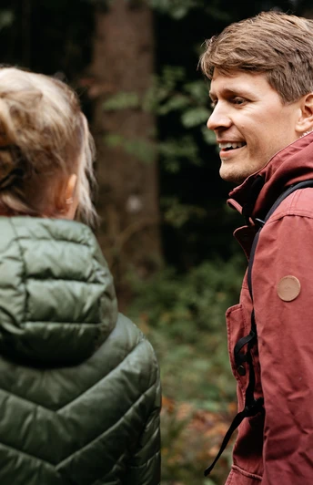 Ein Mann und eine Frau wandern in waldreicher Umgebung, tragen wetterfeste Kleidung.A man and a woman hike in wooded surroundings, wearing weatherproof clothing.En mand og en kvinde vandrer i skovomgivelser iført vejrbestandigt tøj.Een man en een vrouw wandelen in een bosrijke omgeving en dragen weerbestendige kleding.