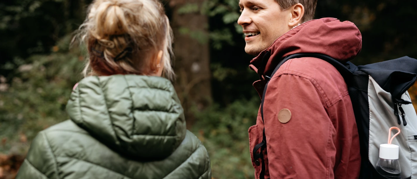 Ein Mann und eine Frau wandern in waldreicher Umgebung, tragen wetterfeste Kleidung.