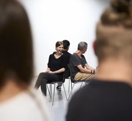 Workshop Team IMPROve Menschen auf Stühlen, Rücken an Rücken, im Dialog. Frau lächelnd, entspannte Gesprächsatmosphäre.