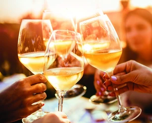 Gläser mit Weißwein werden in einer geselligen Runde bei Sonnenuntergang freudig angestoßen.