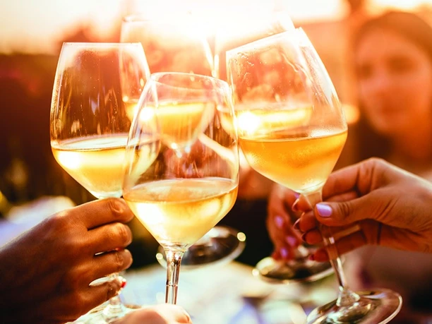 Gläser mit Weißwein werden in einer geselligen Runde bei Sonnenuntergang freudig angestoßen.