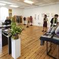 Menschen in einem Ausstellungsraum schauen sich verschiedene Textilien oder Bilder an.