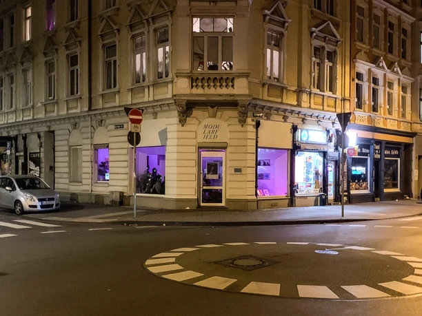 Modularfield Der Eingangsbereich eines Eckhauses bei Nacht, beleuchtet von lilafarbenem Licht.