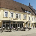 Kupferherz Herford-Pro Herford GmbH.jpeg Ein historisches Gebäude mit gelber Fassade beherbergt ein Café mit Terrasse und weißen Sitzmöbeln.