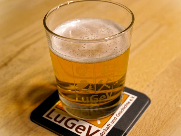 Klosterbier Ein kühles, goldenes Bier in einem Glas auf einem Untersetzer mit "LuGeV" Logo, auf einem Holztisch.