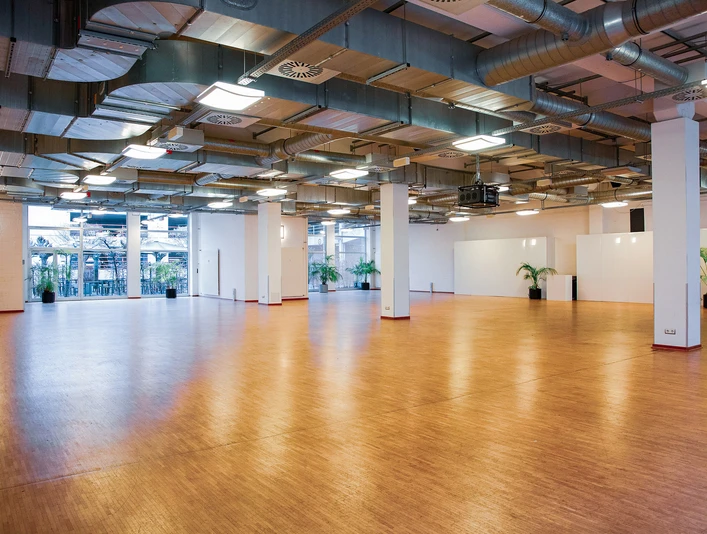 Titelbild (Schlossallee).jpg Großer, leerer Veranstaltungsraum mit Holzfußboden und modernen, industriellen Deckenstrukturen.Large, empty event room with wooden flooring and modern, industrial ceiling structures.